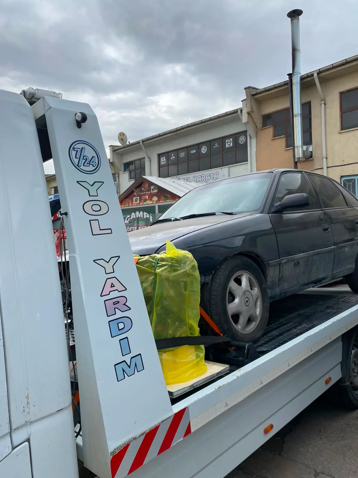 Çekici platformuna bağlanmış siyah sedan otomobil ve kayışlarla sabitlenmiş ekipman