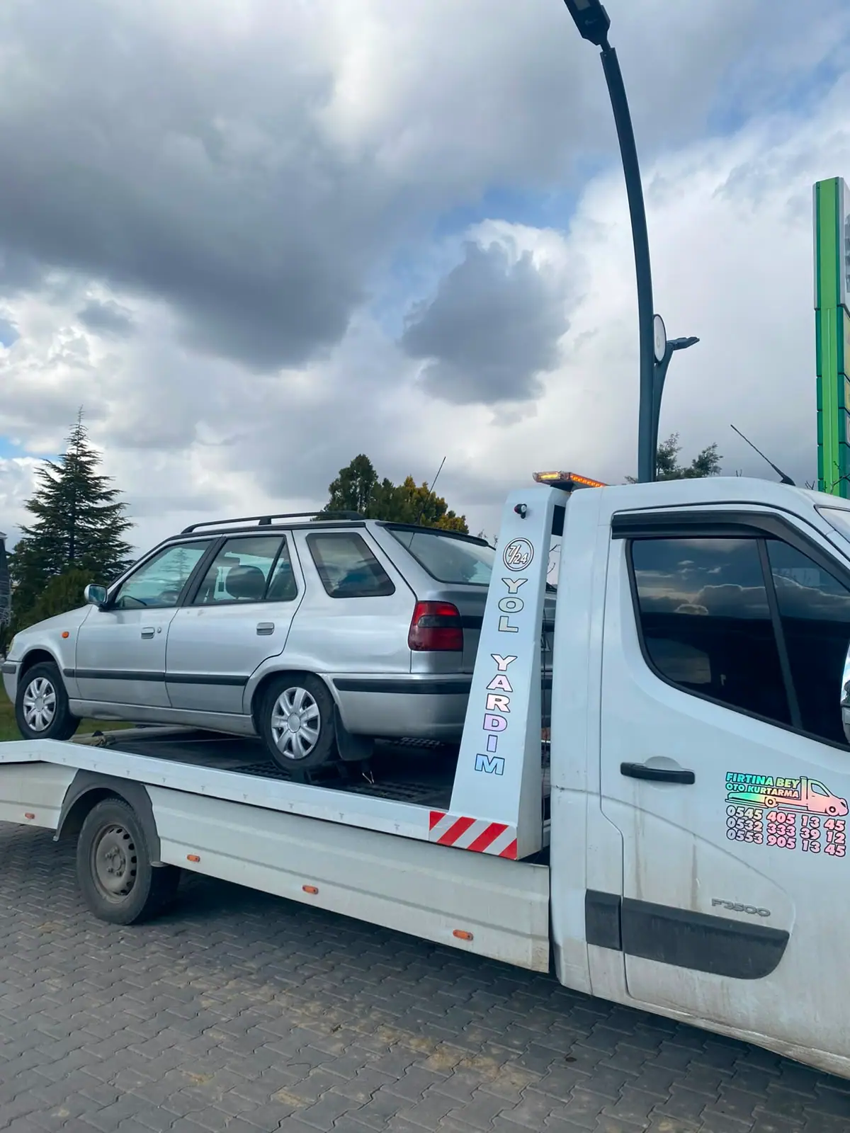 Fırtınabey Oto Kurtarma yazılı 7/24 yol yardım çekicisi ve platformunda taşınan gri station wagon otomobil