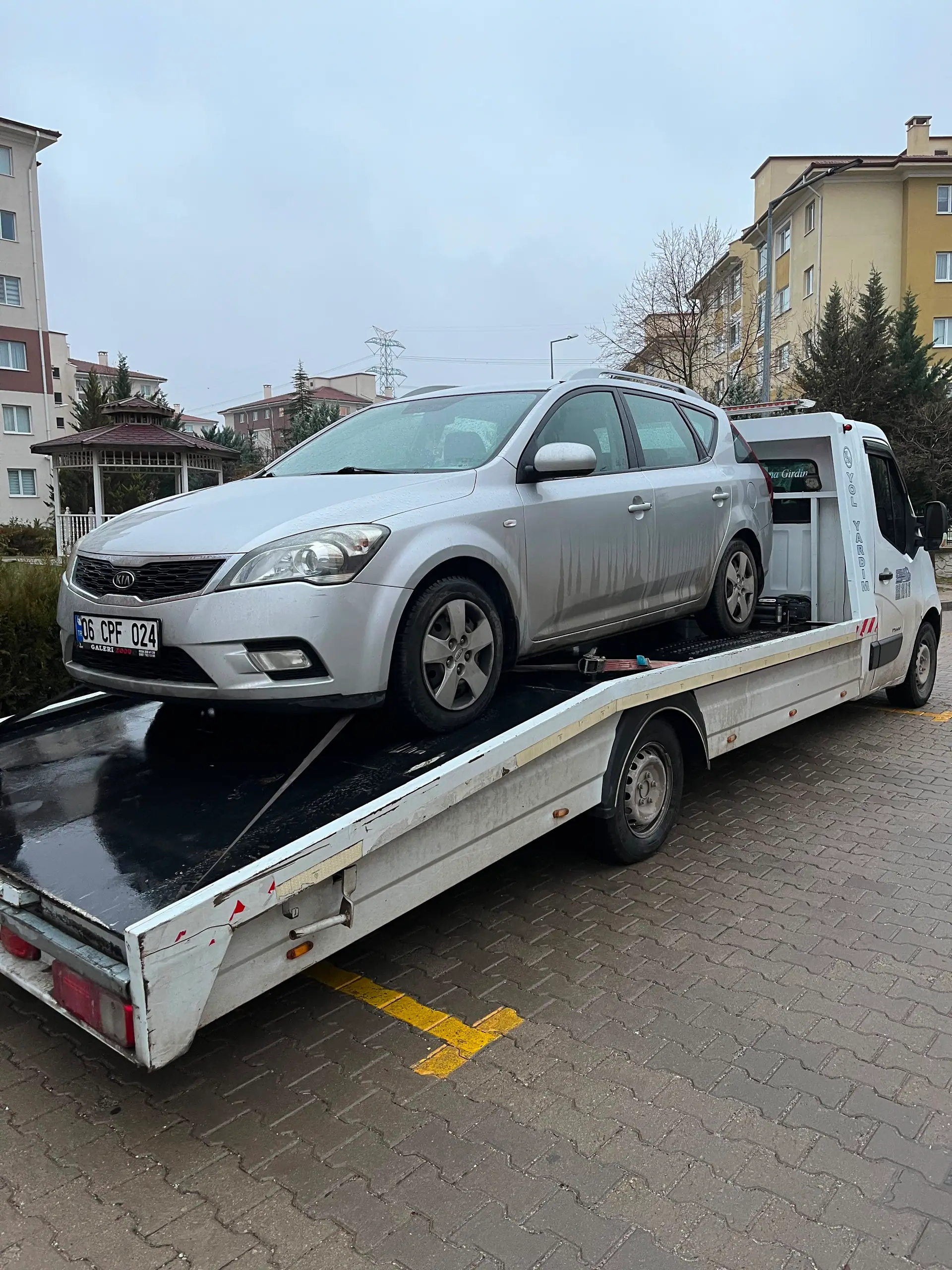 Konut sitesi otoparkında çekici platformuna alınmış gri station wagon otomobil