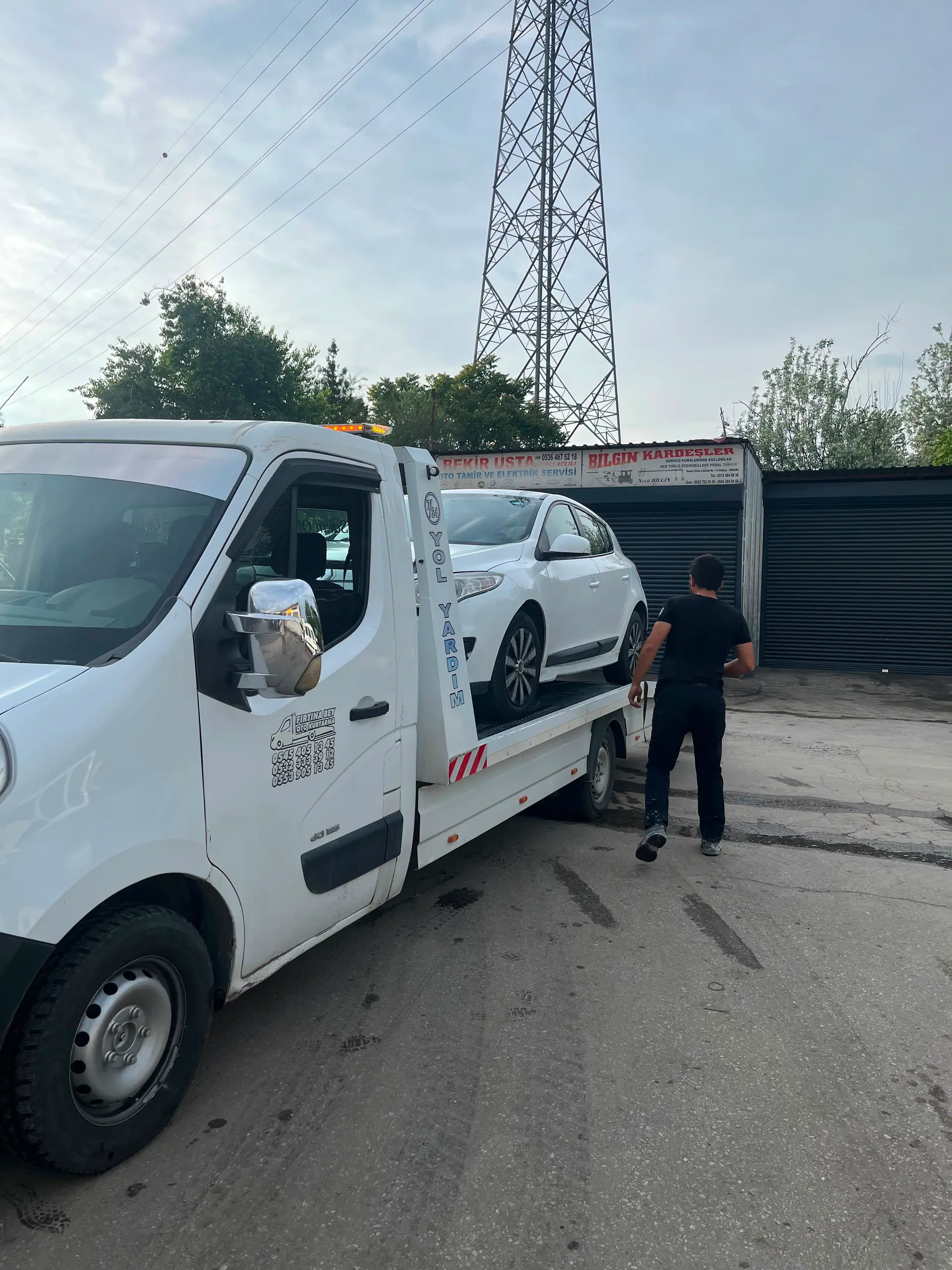 Oto tamir ve elektrik servisi önünde çekiciden indirilen beyaz otomobil ve çalışan görevli