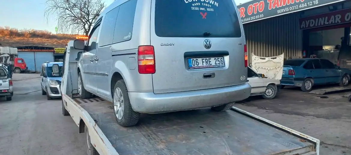 Sanayi sitesindeki oto tamir dükkânları önünde çekici platformuna alınmış gri hafif ticari araç